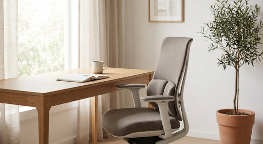 A sleek ergonomic office chair positioned at a tidy wooden desk in a bright, minimalist home office bathed in soft natural light.